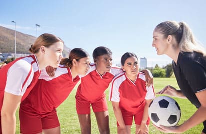 A group of young girls in red and white uniforms are holding a soccer ball.