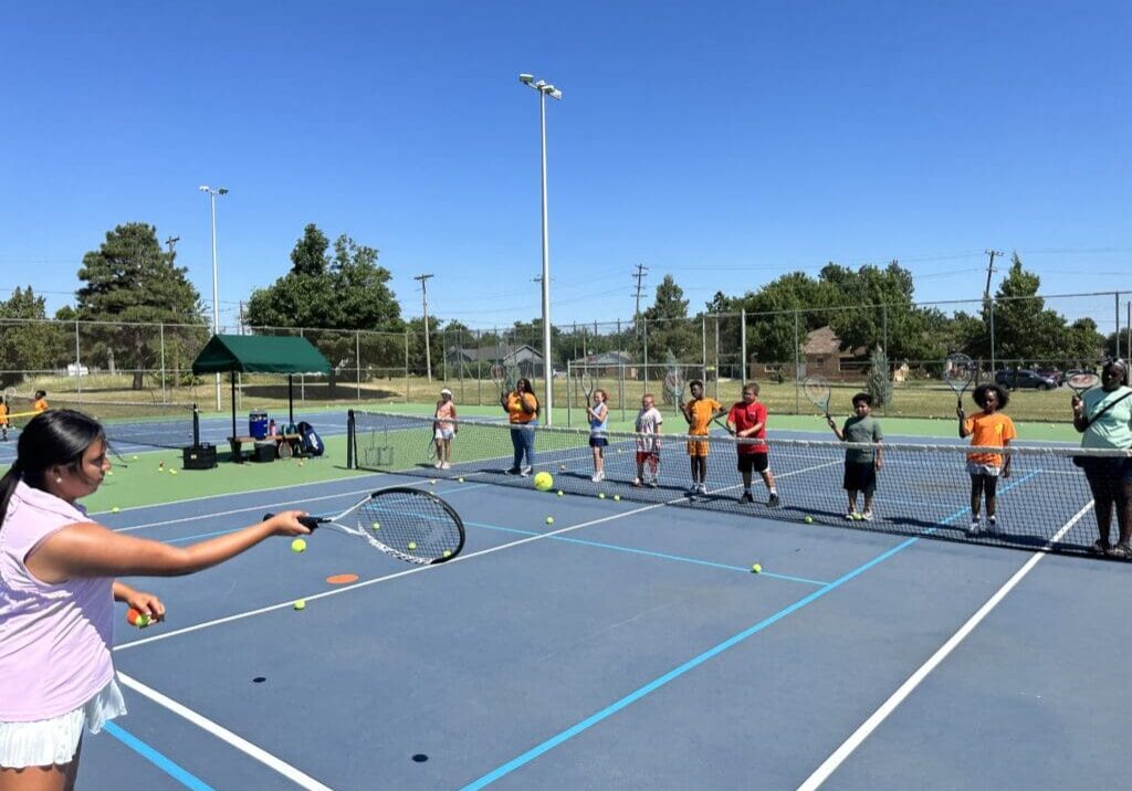 A group of people on a tennis court holding rackets.